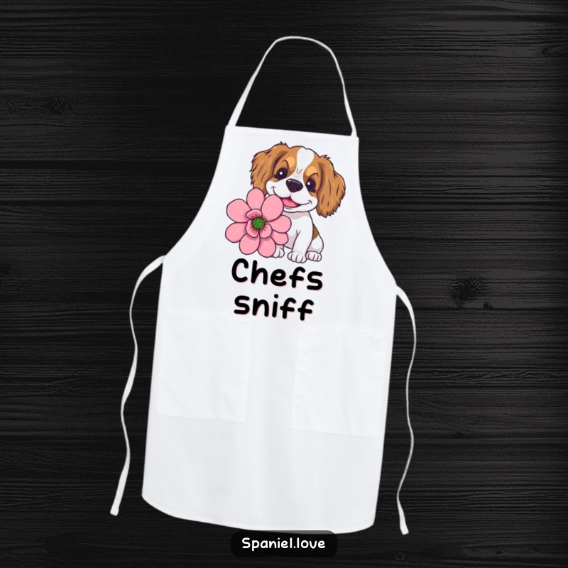 Funny spaniel with a goofy smile sniffing a giant flower, featured on a kitchen apron for cheerful cooks.