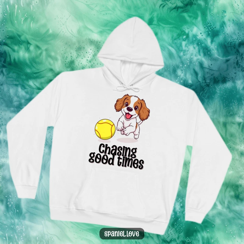 Funny spaniel puppy excitedly chasing an oversized tennis ball, featured on a cozy hoodie, radiating playful energy.